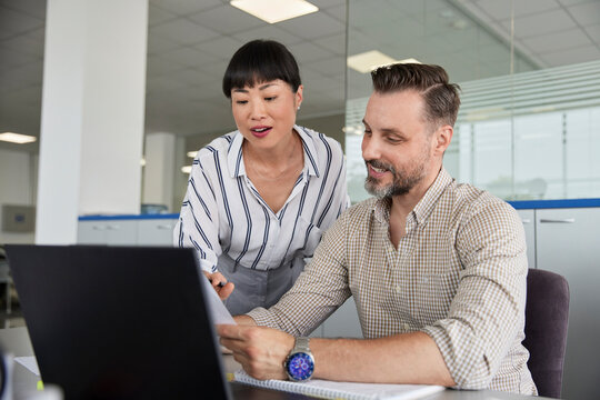 Smiling man explaining colleague over laptop