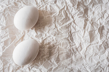 White eggs placed on crumpled paper, creating a minimalist and organic composition. Soft natural light enhances textures, making it ideal for Easter, food photography, and rustic backgrounds