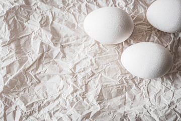White eggs placed on crumpled paper, creating a minimalist and organic composition. Soft natural light enhances textures, making it ideal for Easter, food photography, and rustic backgrounds