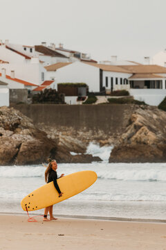 A female surfer with a yellow surfboard walks along the shore i