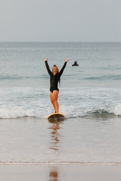 A female surfer rides a small wave and raises her hands in excit