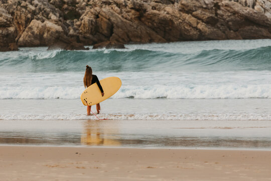 A female surfer with a yellow surfboard walks along the shore i