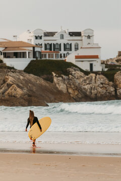 A female surfer with a yellow surfboard walks along the shore i