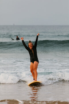 A female surfer rides a small wave and raises her hands in excit
