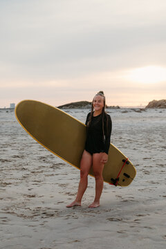A millennial surfer woman poses with her board on the beach at s