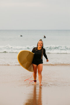 A happy female surfer walks back from the ocean, carrying her bo