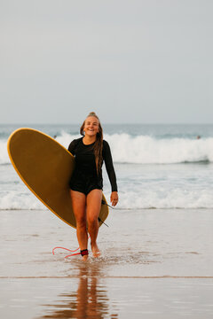 A smiling female surfer walks back from the ocean carrying her b