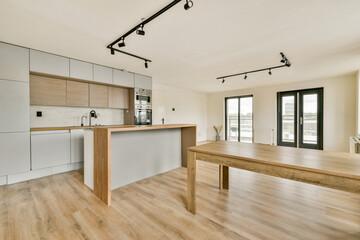 A sleek, modern kitchen featuring light wood and grey cabinetry. The open space, natural light, and minimalistic design create a fresh and inviting atmosphere.