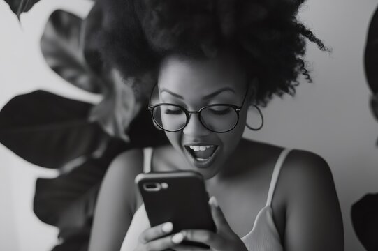 Black and white portrait of a surprised African American woman gasping while reading good news on a smartphone