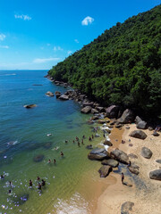 Obraz premium Praia do Cedro, in Ubatuba, Brazil, offers an untouched tropical haven with crystal-clear waters and golden sands nestled between lush green hills. The rocky shoreline enhances the charm.