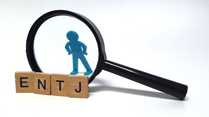 .Wooden blocks spelling "ENTJ," with a small toy figure placed behind a magnifying glass. ENTJ is one of the 16 personality types identified by the Myers-Briggs Type Indicator or MBTI.