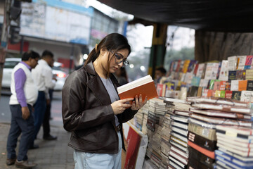 A college student reading book standing on the pavement beside street