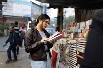 A college student reading book standing on the pavement beside street