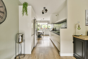A stylish minimalist kitchen featuring sleek cabinetry, wooden flooring, and elegant plants. The layout emphasizes functionality and modern design aesthetics.