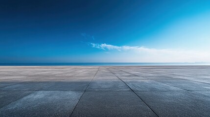 Empty concrete expanse meets tranquil ocean under a vibrant blue sky. Ideal for showcasing products, travel, or serenity, evokes peace and vastness.