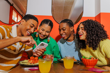 Happy friends sharing funny content on smartphone at restaurant