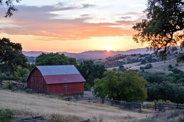 Red barn stands on hill at sunset over california countryside