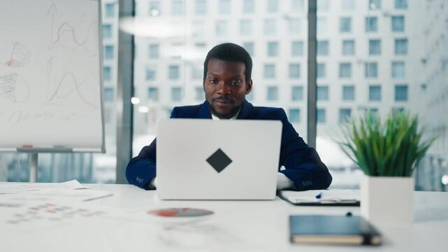 Frontal portrait of financial analyst or CEO Manager in office with laptop. African American male person closing notebook and leaning on chair back, rejoicing by end of working day or good project