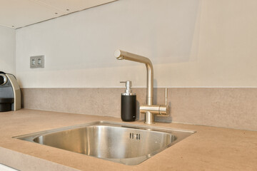 A sleek and minimalistic kitchen design featuring a stainless steel sink, elegant faucet, and smooth stone countertop, creating a stylish cooking space.