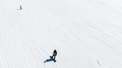 Aerial view of a person snowboarding down a slope. Behind him, on the ski slope with lots of snow,...
