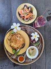 The Thai set meal includes omelets over rice, spicy seafood salad, butterfly pea drink, and fruit.