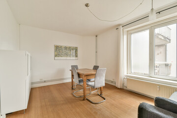 A modern interior showcasing a dining area with a minimalist style. Features a simple table, chairs, and a large window allowing natural light.