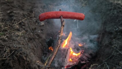 Grilled sausage on the background of a campfire. adventure, travel, tourism and camping concept