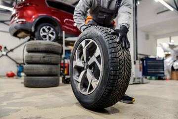 Close up of mechanic rolling tire at car repair workshop.