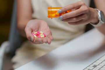 Woman pouring pink and white capsules from pill bottle into hand