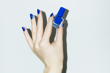 Hand with royal blue manicure holding beauty product nail polish
