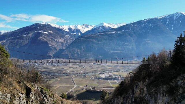 Saillon, Switzerland - 15 February 2025: Tourists Walking Across the Passerelle &agrave; Farinet, a Wooden Bridge Above the Salentse Gorge with Views of the Swiss Alps on a Beautiful Sunny Day