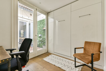 A modern workspace featuring sleek furniture, a comfortable chair, and a stylish rug. Natural light floods the space from large windows, enhancing the minimalist design.