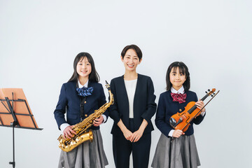 サックスとバイオリンを持った女子学生グループと女性教師