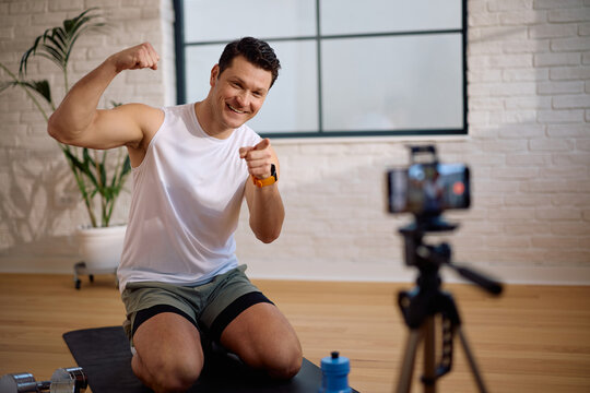 Happy coach flexing his bicep while recording vlog at his fitness studio.