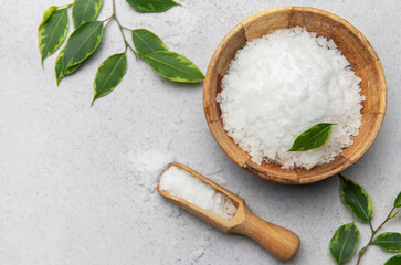 Magnesium flakes in wooden bowl with scoop and green leaves on gray background