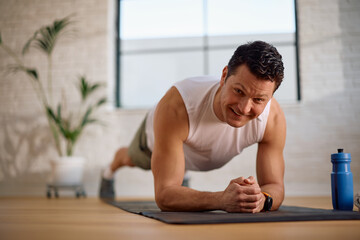 Happy athletic man doing plank exercise and looking at camera.