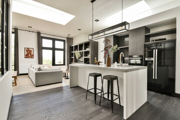 A contemporary kitchen featuring sleek cabinetry, open space, and stylish bar stools, complemented by natural light from skylights and large windows.