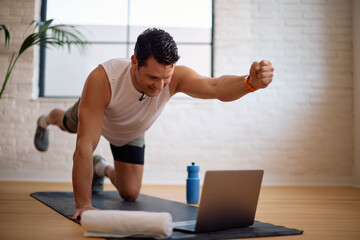 Happy athlete working out while watching exercise tutorial on laptop.