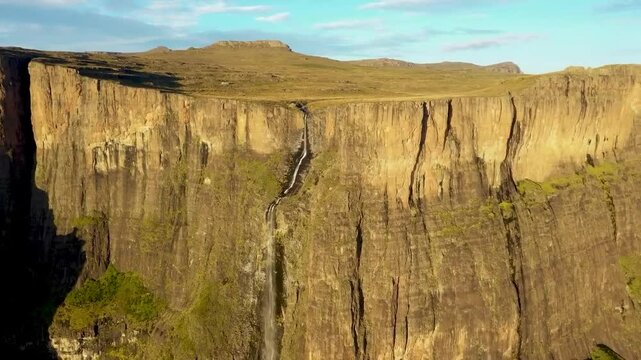 Aerial drone footage flying closer to Tugela Falls waterfall in Sauth Africa Royal Natal park during a sunny summer day. The narrow river is falling down from a very tall and steep brown cliff.