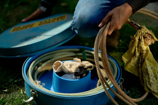 A person handling coiled ropes and tools in a blue container on grass, wearing jeans and gloves. Brandenburg, Germany
