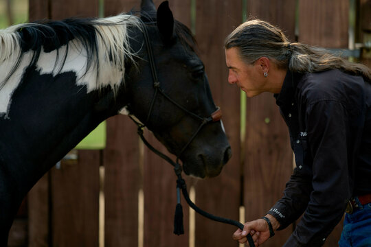 Person with long hair gently interacting with a black and white horse near a wooden fence. Brandenburg, Germany