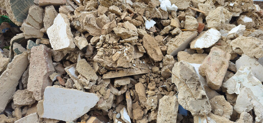 Pile of construction debris; broken bricks, chunks of concrete, scattered wood pieces, and crushed plaster mixed with dirt and dust;