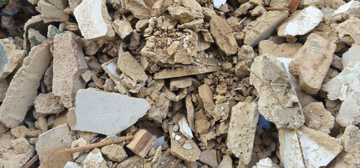 Pile of construction debris; broken bricks, chunks of concrete, scattered wood pieces, and crushed plaster mixed with dirt and dust;