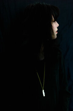 Woman in dark clothing and neckless looking away against a dark background Berlin, Germany