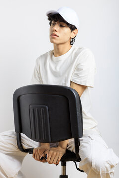 Androgynous person dressed in white sitting on chair over white wall