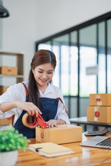Young woman happily packing boxes with tape at a modern home office workspace surrounded by shipping supplies