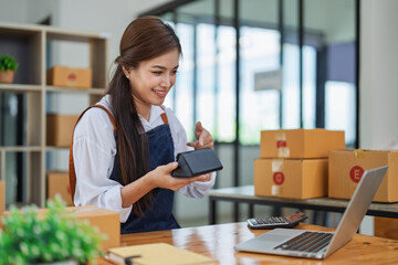 Young woman engaged in online business while packing delivery product at a wooden table while...