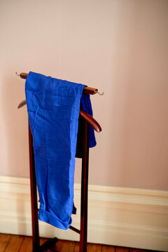 Blue pants hanging on a wooden clothing valet in a softly lit hotel room. Hauts-de-France, France