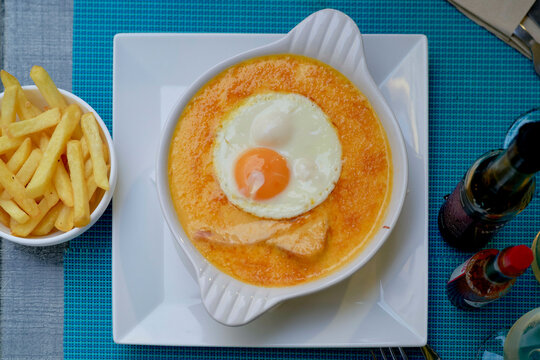 French croque monsieur topped with a fried egg, served with golden fries in a white dish. Hauts-de-France, France