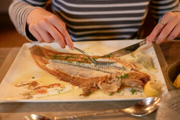 Woman with funny nail design enjoying a meal of grilled fish with herbs on a square white plate at a table. Hauts-de-France, France